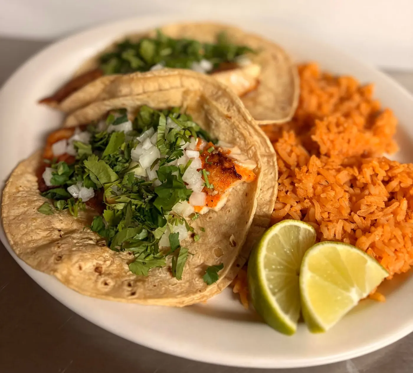 Three corn tortilla tacos with cilantro and onion, rice and lime wedges